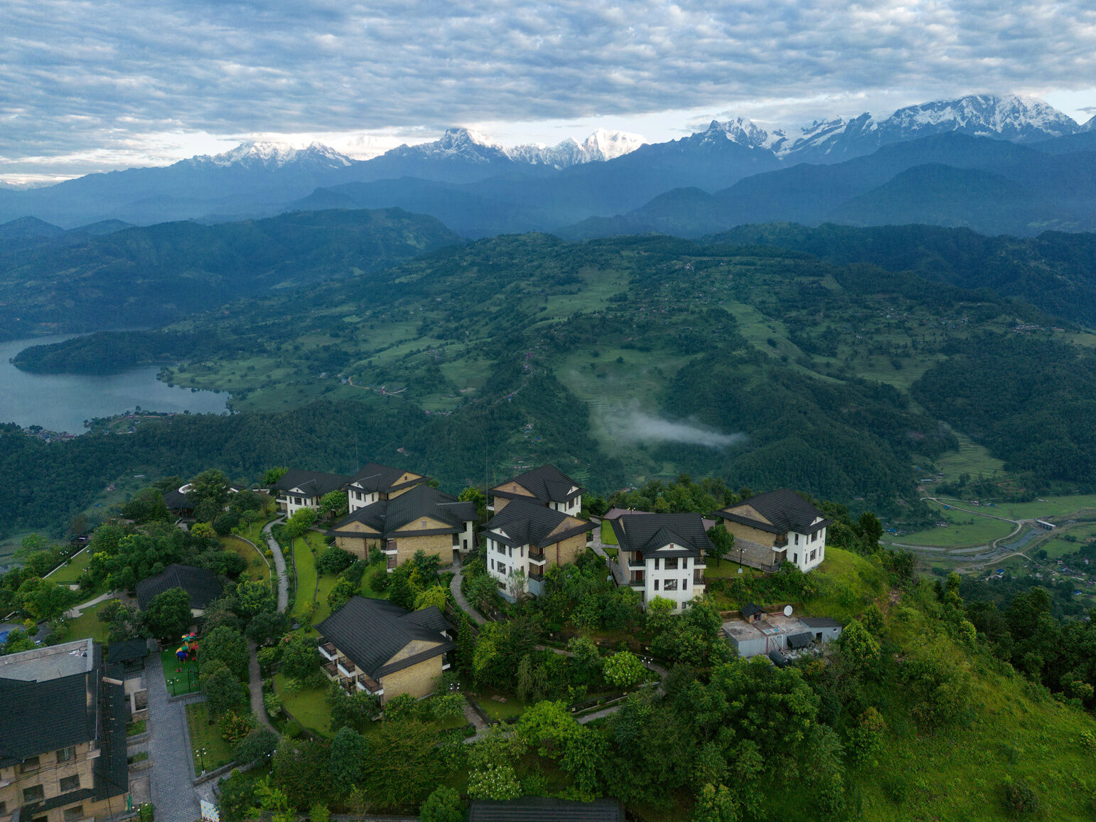 Aerial view of Rupakot Resort on its green hilltop, with lakes and the Annapurna range beyond