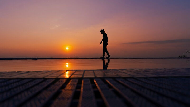A person walking along the edge of the infinity pool at sunset